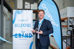 Man smiling at a corporate grand opening event, holding ribbon-cutting scissors in front of a CryoPDP banner, captured by Light Planning Media’s event photography services.