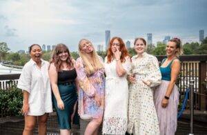 Group of women posing playfully at an outdoor event with the Brisbane skyline in the background, captured by Light Planning Media’s event photography services
